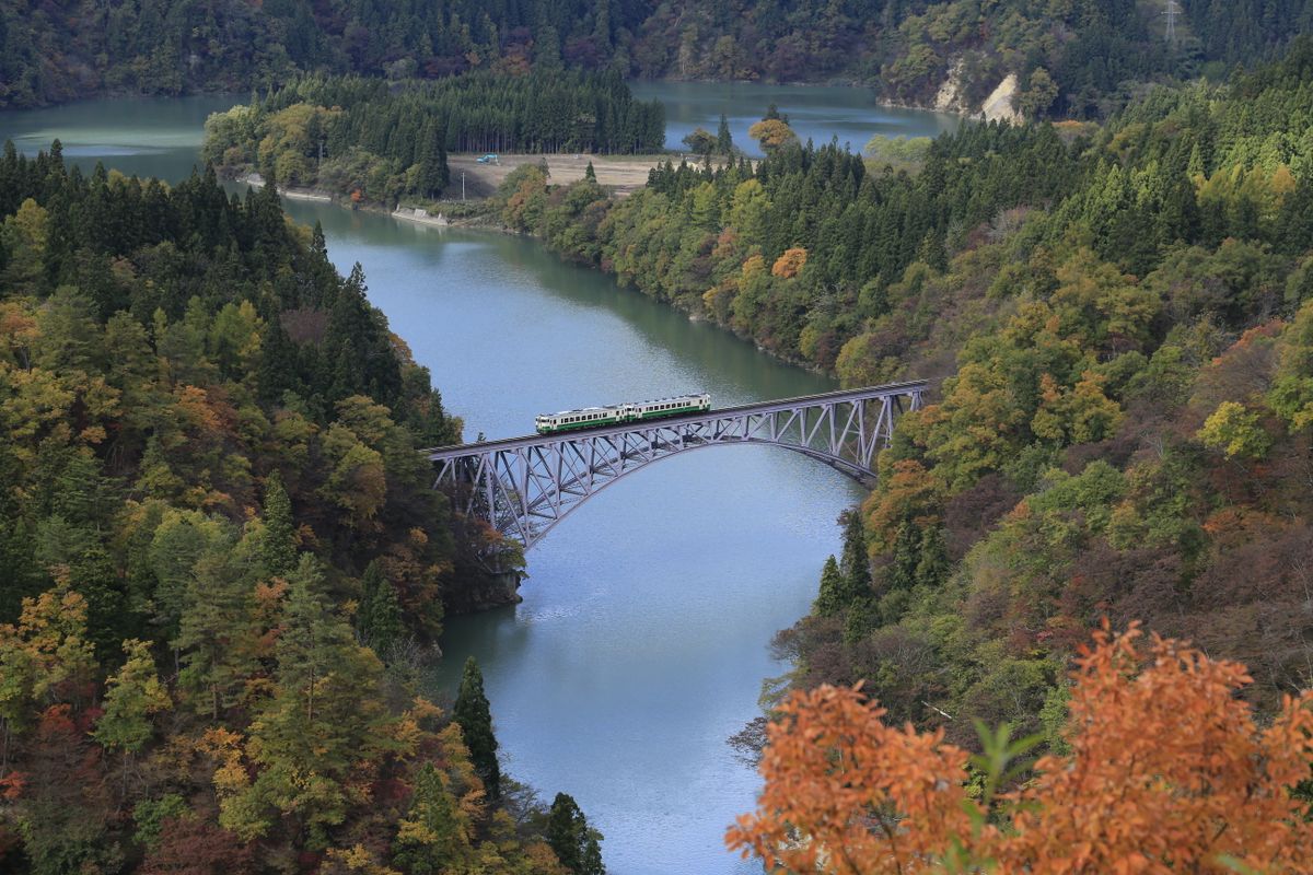 The Tadami Line train crossing the famous bridge over the Tadami River surrounded by autumn foliage — Fukushima Prefecture