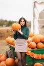 一位女士在户外秋季节日上与南瓜合影，展示了充满活力的秋季氛围