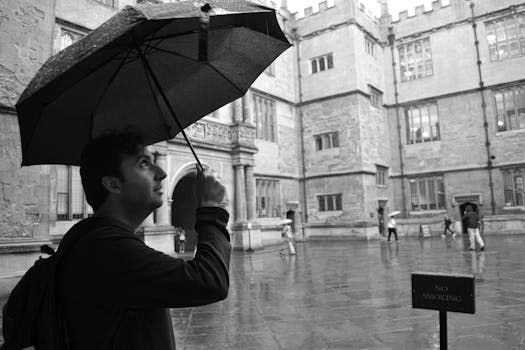 A man holding an umbrella in the rain at an Oxford courtyard, England.
