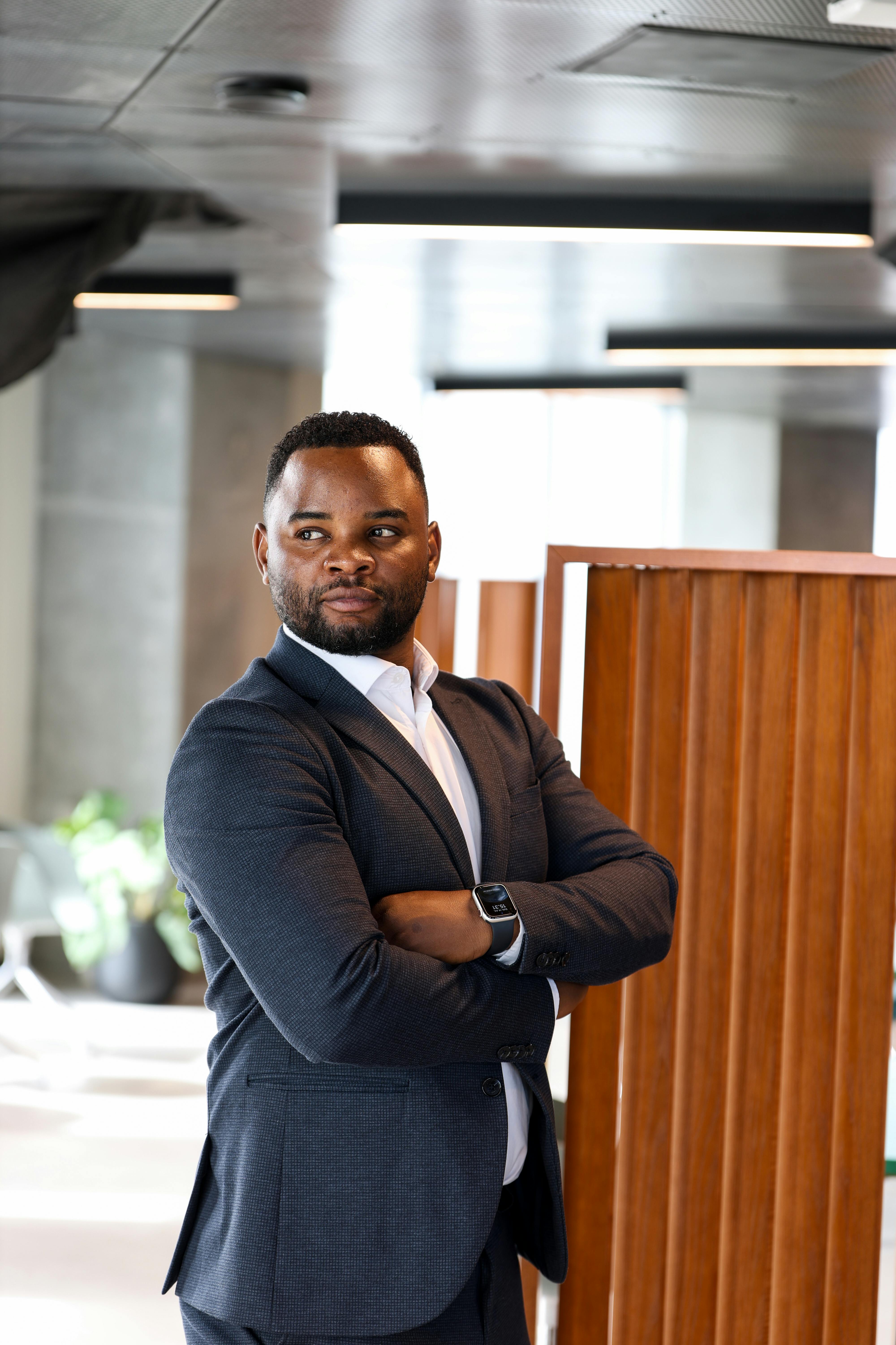 A confident businessman standing in an elegant, modern office with arms crossed.