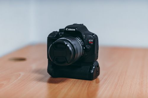 Free Close-up of a Canon DSLR camera with lens cap, placed on a wooden table indoors. Stock Photo