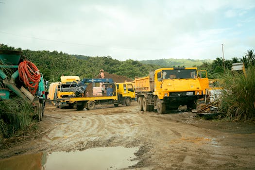 A bustling construction site with yellow trucks and machinery set in a green rural landscape.