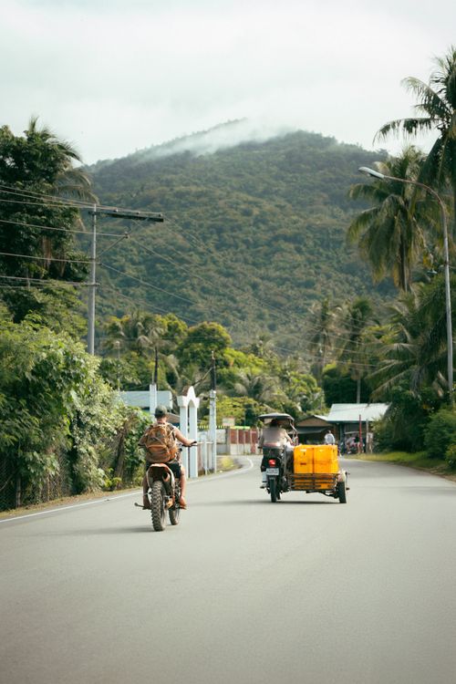 Free Two motorcyclists ride through a tropical road with lush mountains in the background. Stock Photo