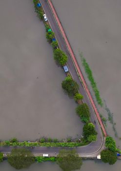 Top-down aerial view of a road partially submerged during a flood, surrounded by water and greenery.