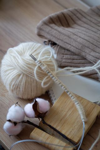 Cream yarn ball with needles beside raw cotton bolls — olga Volkovitskaia on Pexels