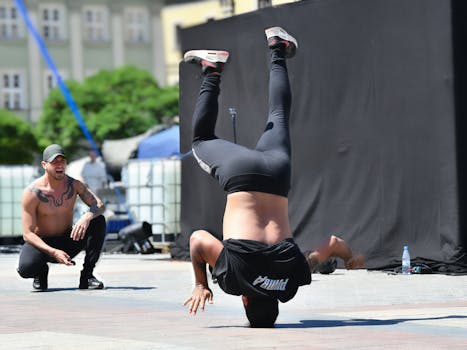 Street dancer executing a headstand during an outdoor breakdance show with a cheering audience.