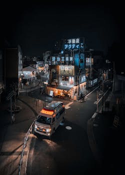 Street view of Tokyo at night featuring a neon-lit izakaya and an ambulance in motion.