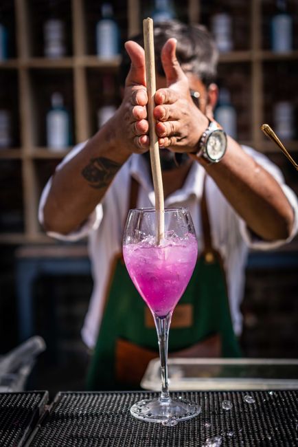 Bartender skillfully mixes a vibrant purple cocktail at an indoor bar setting.