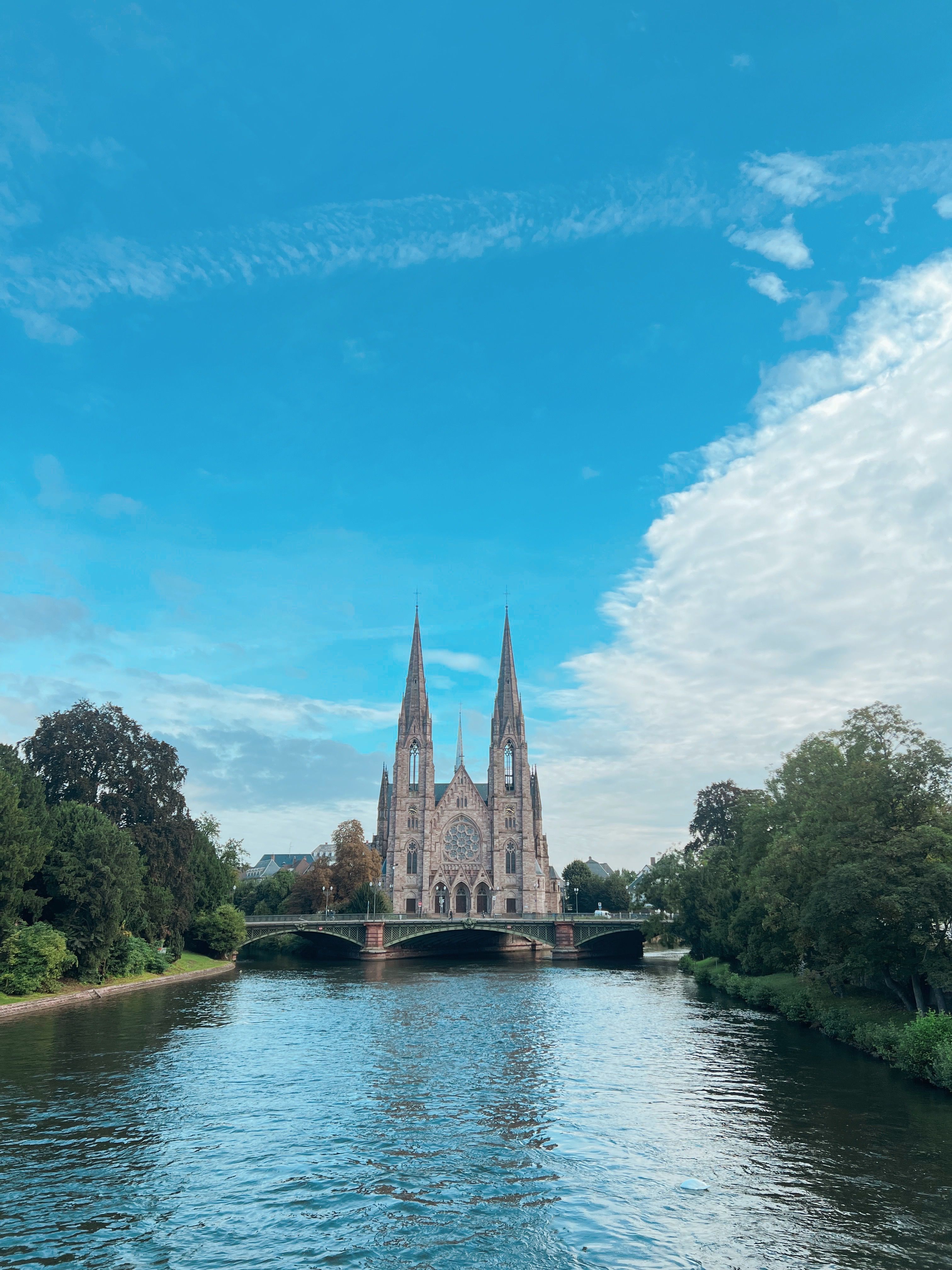 St Nicholas Church with tall spires reflected in the river under a vibrant blue sky.