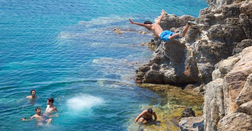 Free A group of friends enjoying cliff diving and swimming in the clear waters at Al Huwariyah, Tunisia. Stock Photo