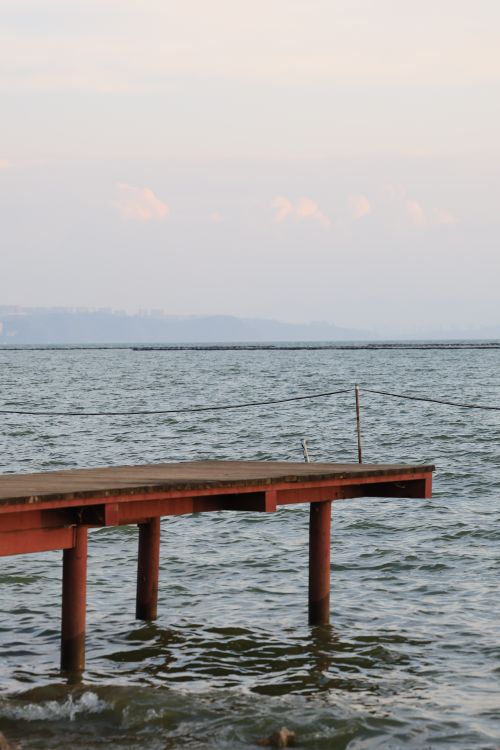 Free A solitary wooden pier stretches into calm sea waters under a serene sky. Stock Photo