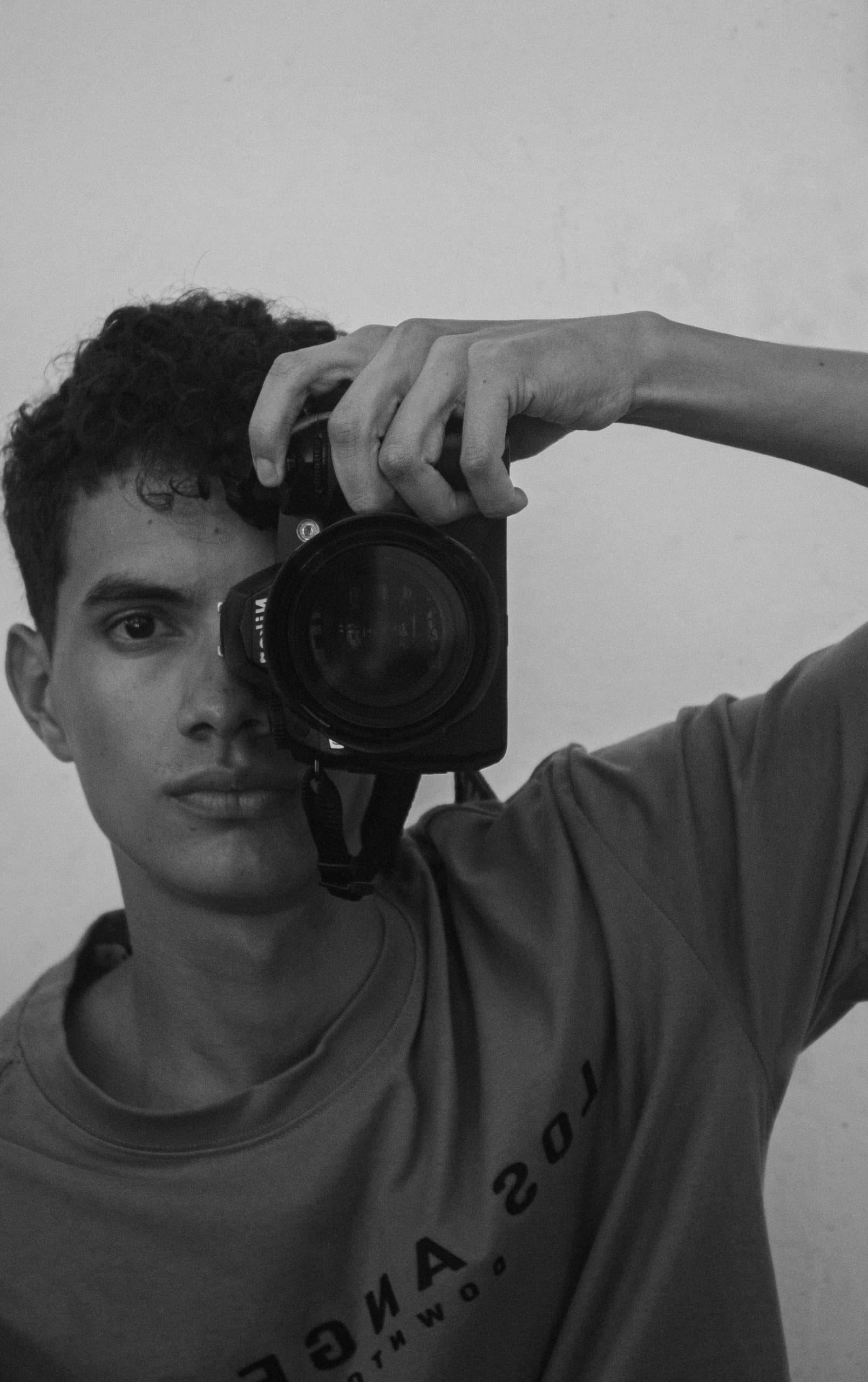 Artistic black and white portrait of a young male photographer holding a camera.