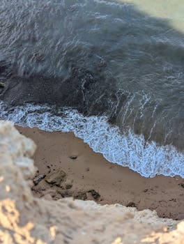 A scenic aerial shot of a sandy beach in Spain, with gentle waves lapping against the shore.