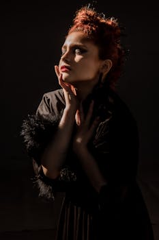 在戏剧性的照明下，一位身穿黑色礼服的美丽女人映衬在黑暗的背景中