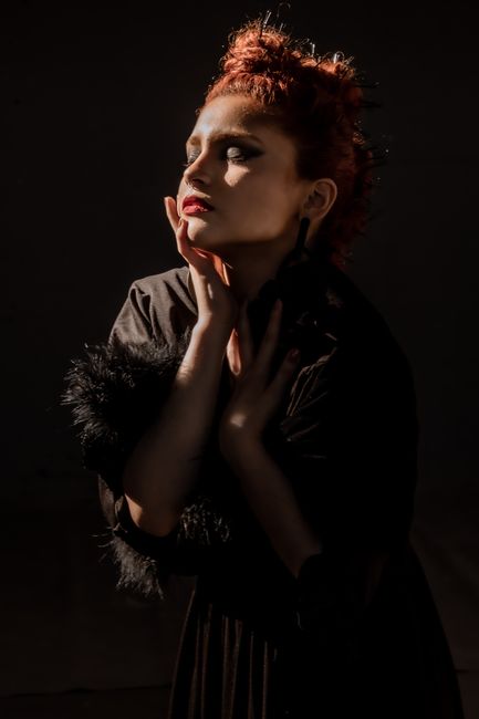 Beautiful woman posing in dramatic lighting wearing a black dress against a dark background.
