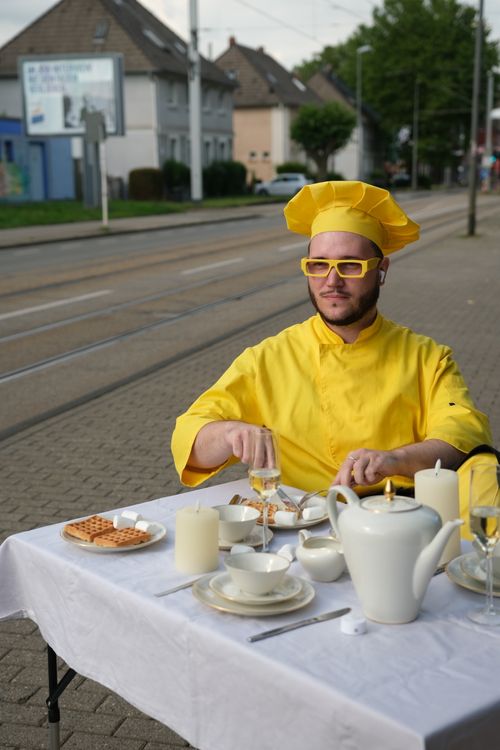 Free A chef in yellow attire sits at an outdoor table having tea with waffles and tea set. Stock Photo