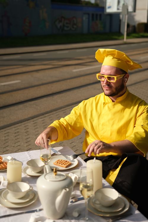 Free Bearded chef in bright yellow attire enjoys waffles at an outdoor picnic table setting. Stock Photo