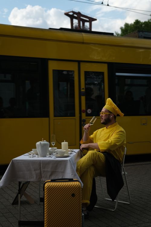 Free A person in yellow attire enjoying a drink at a table by a yellow tram outdoors. Stock Photo