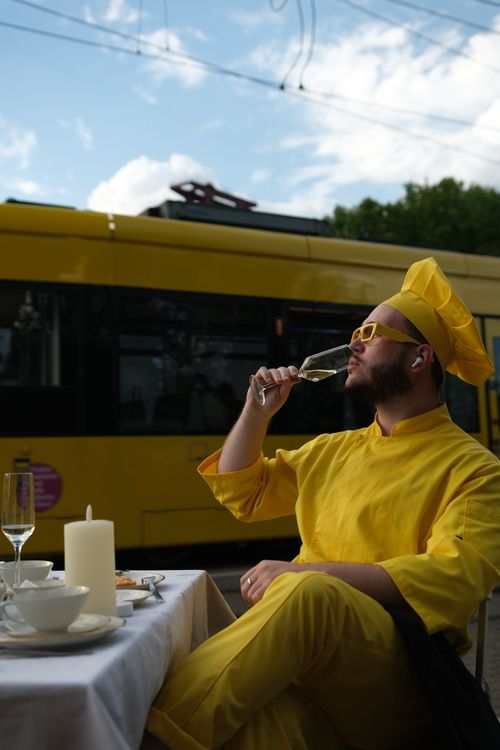 Free A chef in yellow attire savors a drink outdoors by a passing yellow tram. Stock Photo