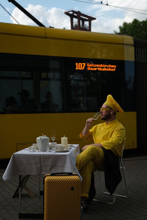 Free A bearded man in yellow attire enjoys a drink by a passing tram in Essen, Germany. Stock Photo