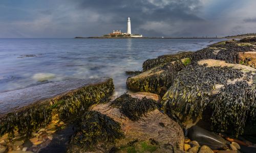 Free Scenic coastal view with lighthouse and rocky shoreline under dramatic sky. Stock Photo