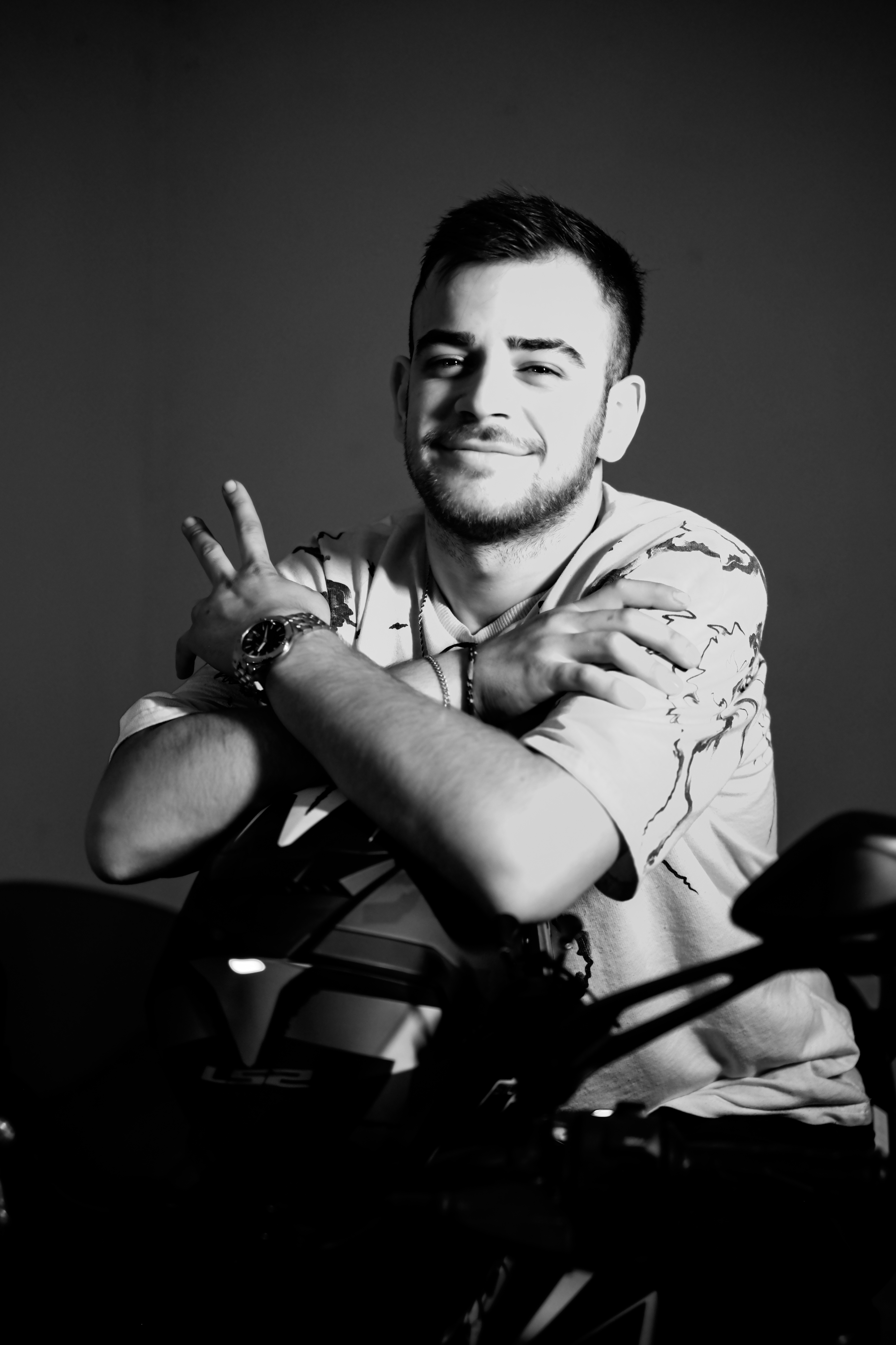 A stylish black and white portrait of a smiling man leaning on a motorcycle indoors.