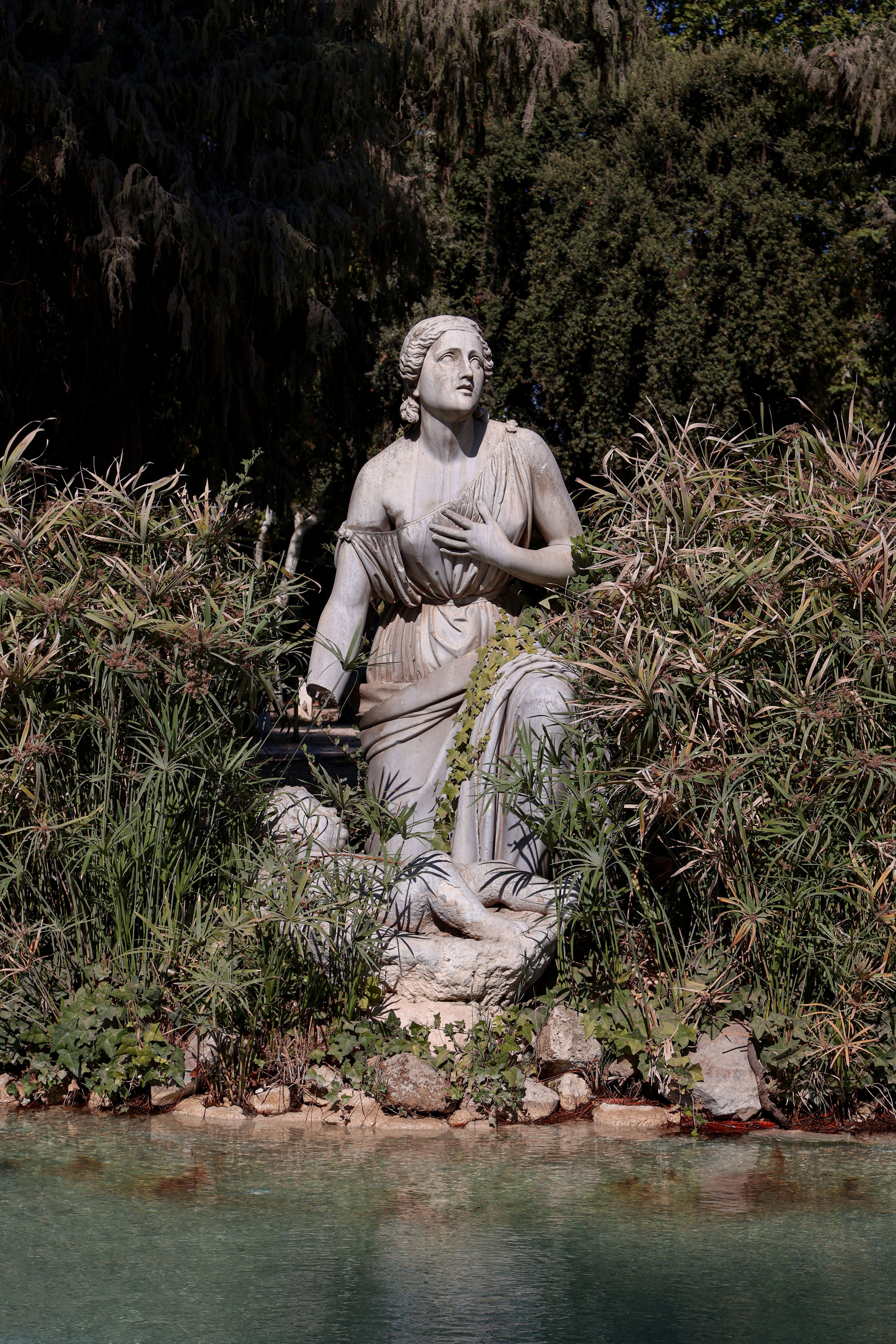 Fotomural Elegante estatua de piedra rodeada de vegetación en un sereno parque romano.