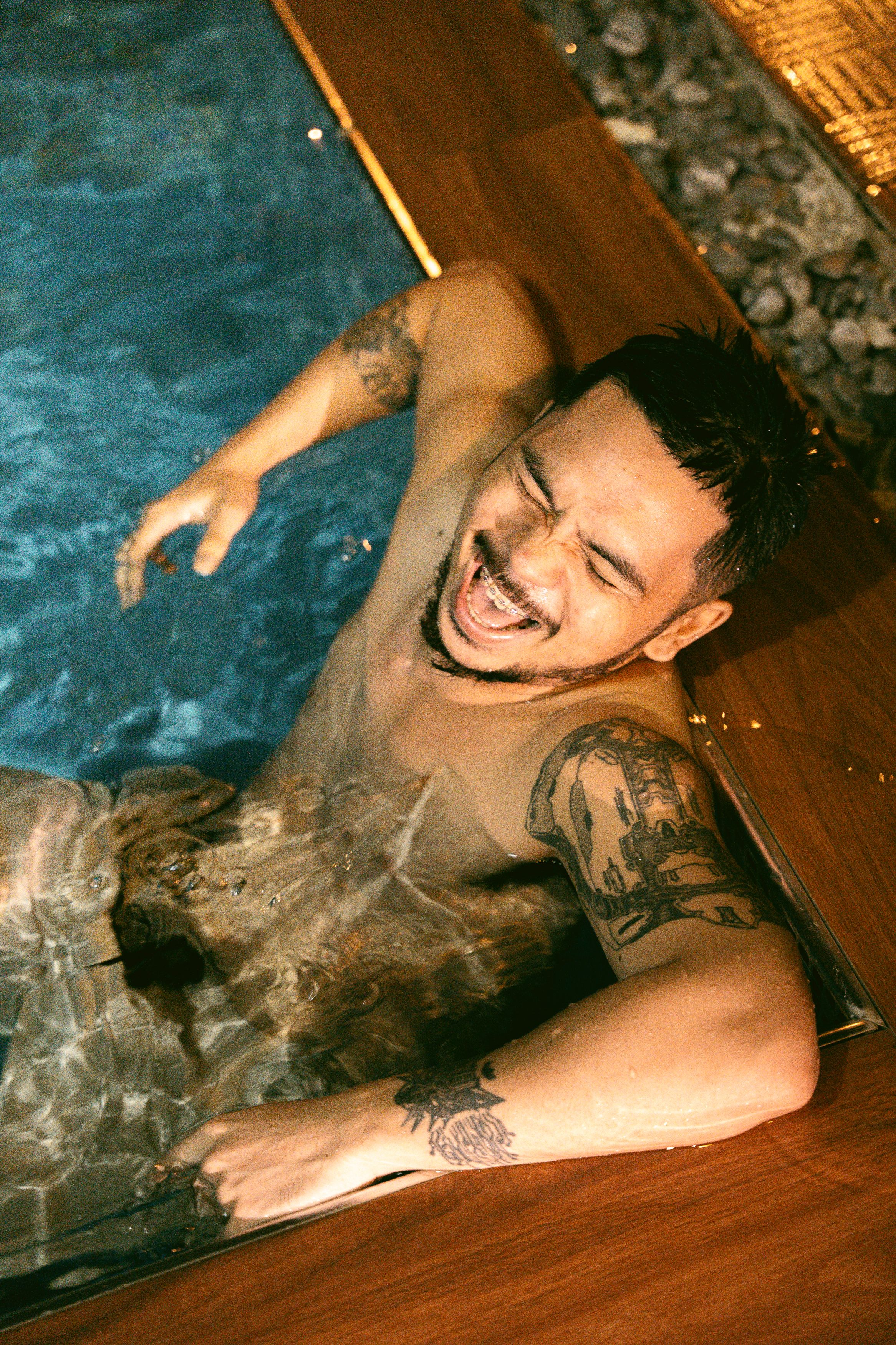 Smiling man with tattoos relaxes in a modern pool, showcasing joy and relaxation.