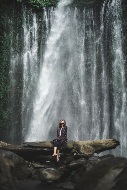 A serene scene featuring a woman at a waterfall in West Nusa Tenggara, Indonesia.