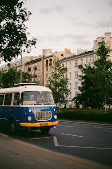 A retro blue and white bus on a Warsaw street with old buildings in the background.