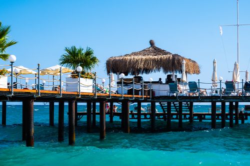 Free Sunny beach resort pier with loungers and umbrellas over crystal clear blue sea, perfect summer escape. Stock Photo