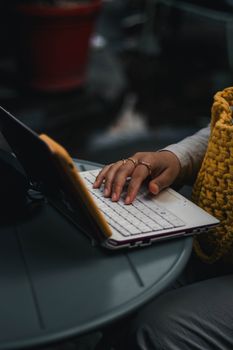 Person typing on a laptop at an outdoor cafe table with warm clothing. Perfect for remote work themes.