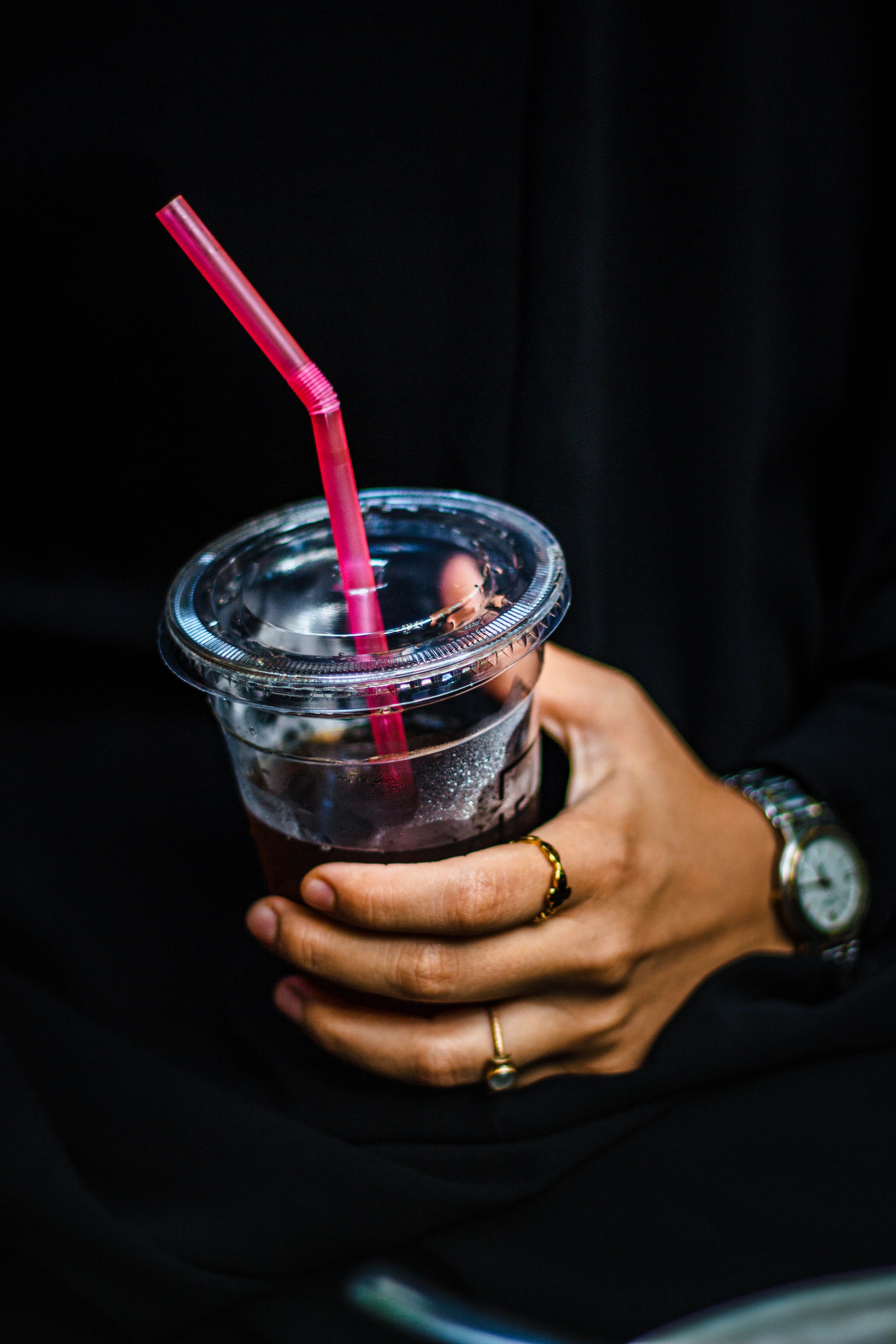 A hand holds an iced drink in a clear cup with a pink straw.