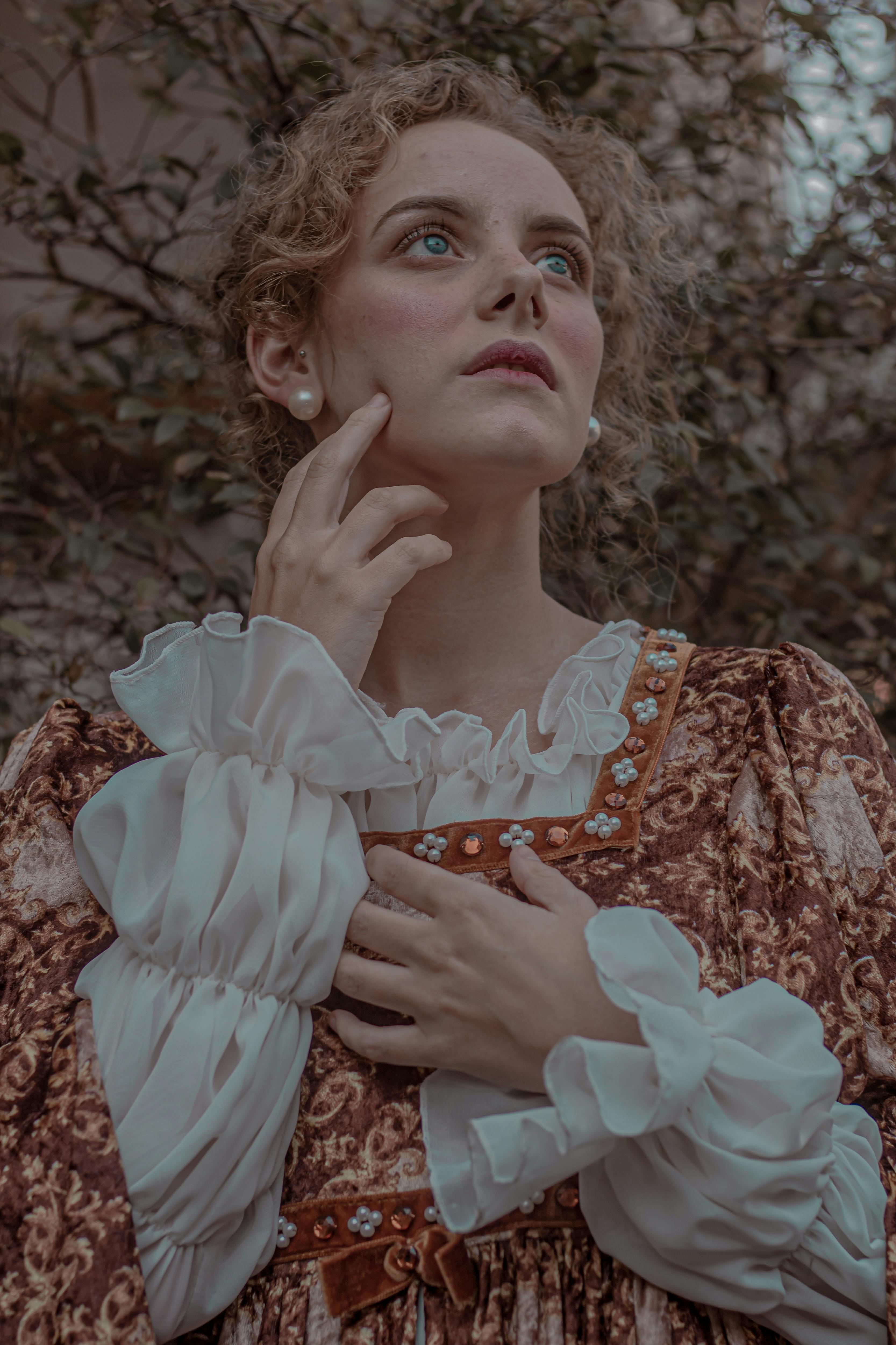 一名身穿复古服装的女子若有所思地在户外摆着姿势，营造出一种喜怒无常的艺术氛围