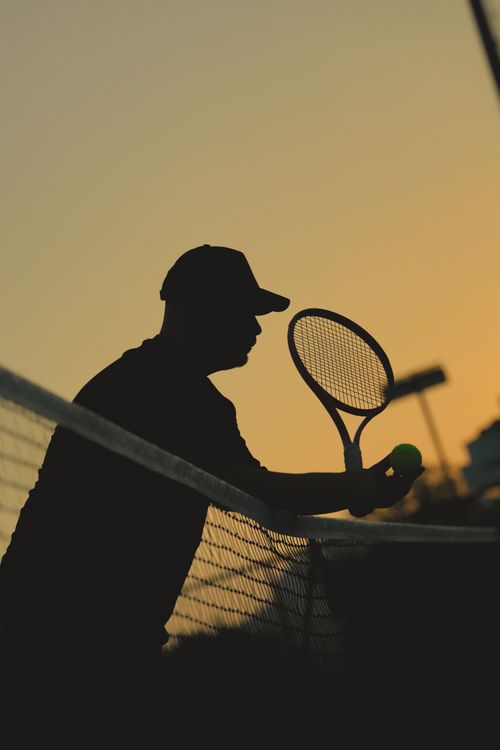 Free Tennis player silhouette holding a racket and ball against a vivid sunset sky. Stock Photo
