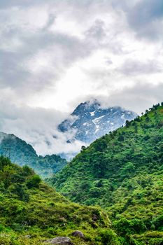 Serene landscape of a majestic mountain under cloudy skies with lush green foliage.