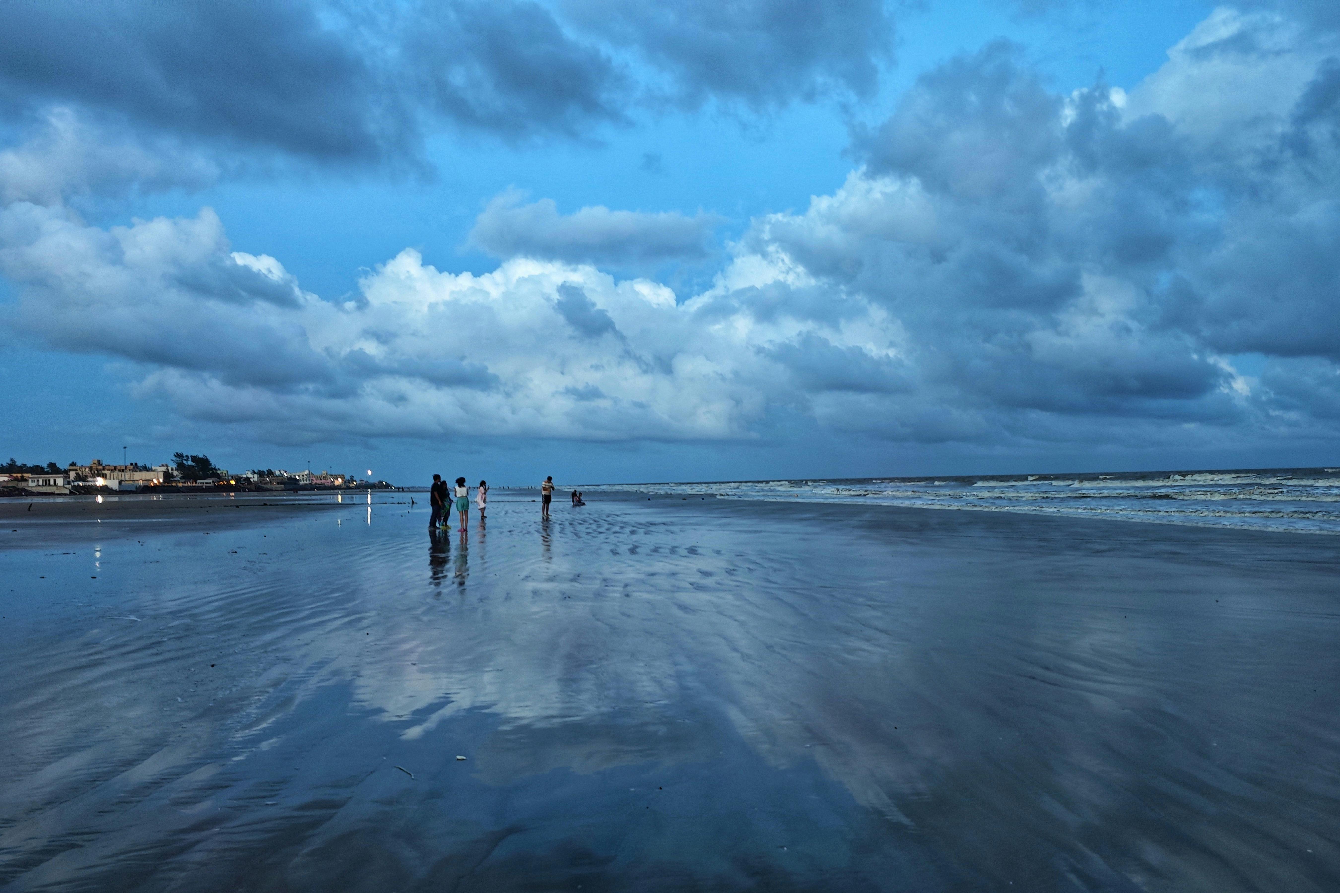 Dramatic cloudy sky reflected on the serene Mandarmani beach in India with people enjoying the scene.