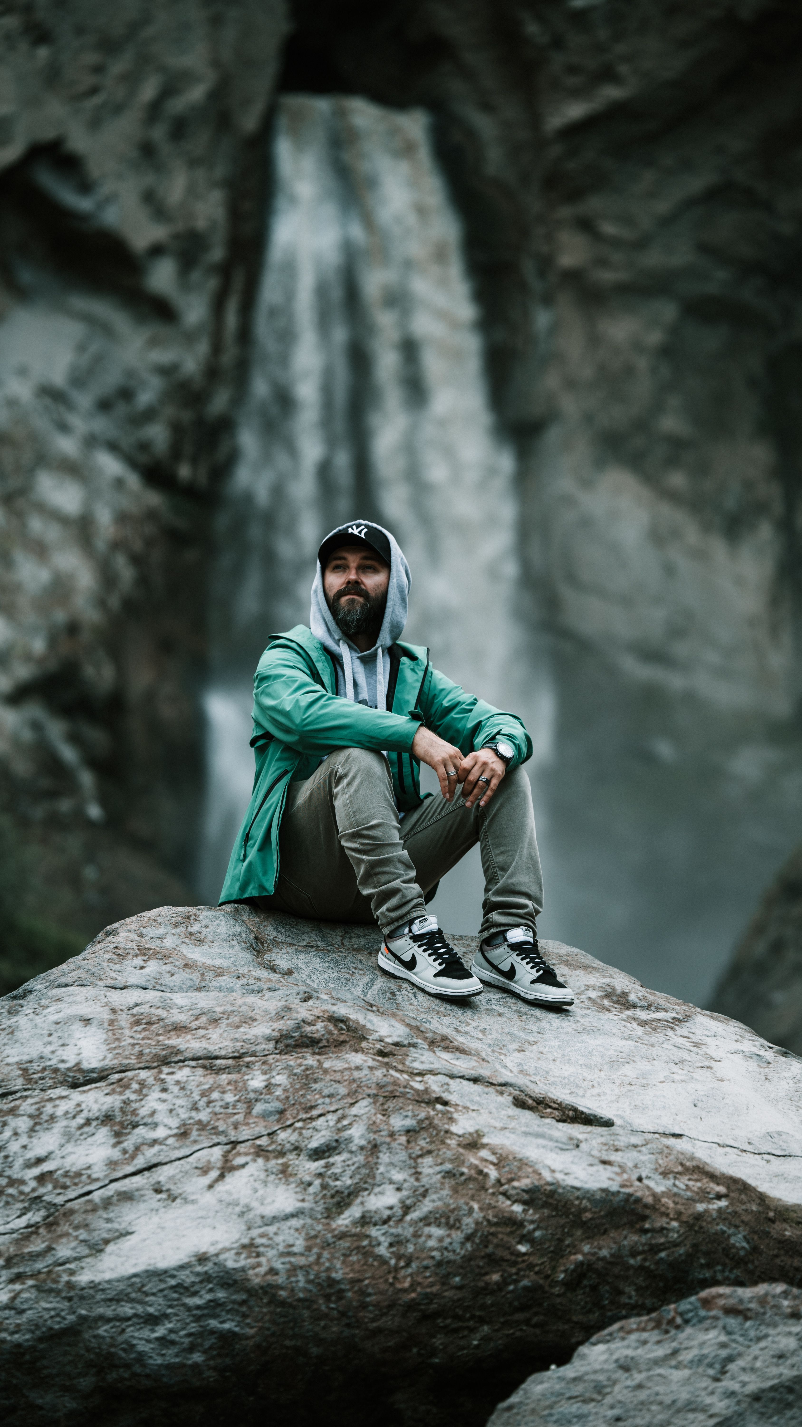 Man in casual clothing sitting by a waterfall, enjoying nature's tranquility.
