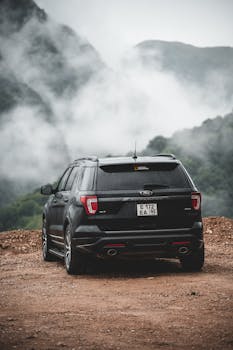 A black SUV parked on a dirt road amidst misty mountains.