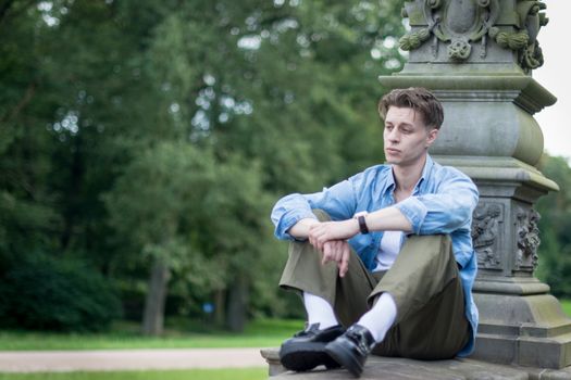 A young man sits pensively on a stone ledge outdoors.