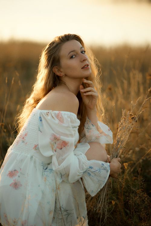 Free A tranquil portrait of a woman in a white dress surrounded by golden grasses. Stock Photo