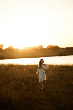 Young woman in a white dress enjoying a sunset by the water in nature.