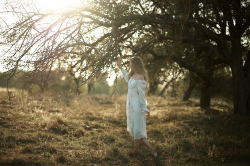 Free Woman in white dress enjoying sunlight in meadow under a tree. Stock Photo