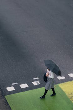 Aerial view of a woman with an umbrella crossing a rainy street in Port Moody, Canada.