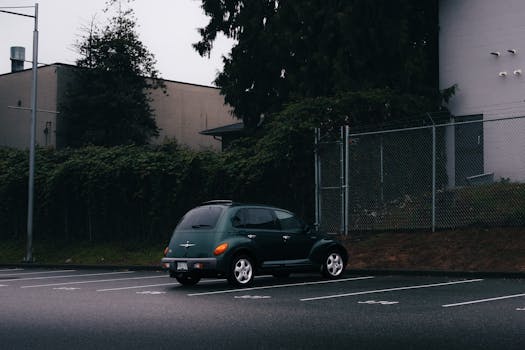 A vintage car parked in a misty, empty lot by lush greenery in Port Moody, BC.
