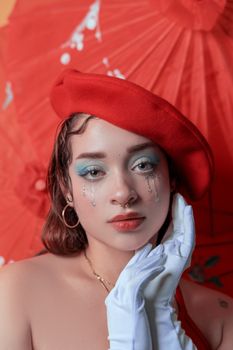 Portrait of a stylish woman in red beret with blue makeup and pearl details.
