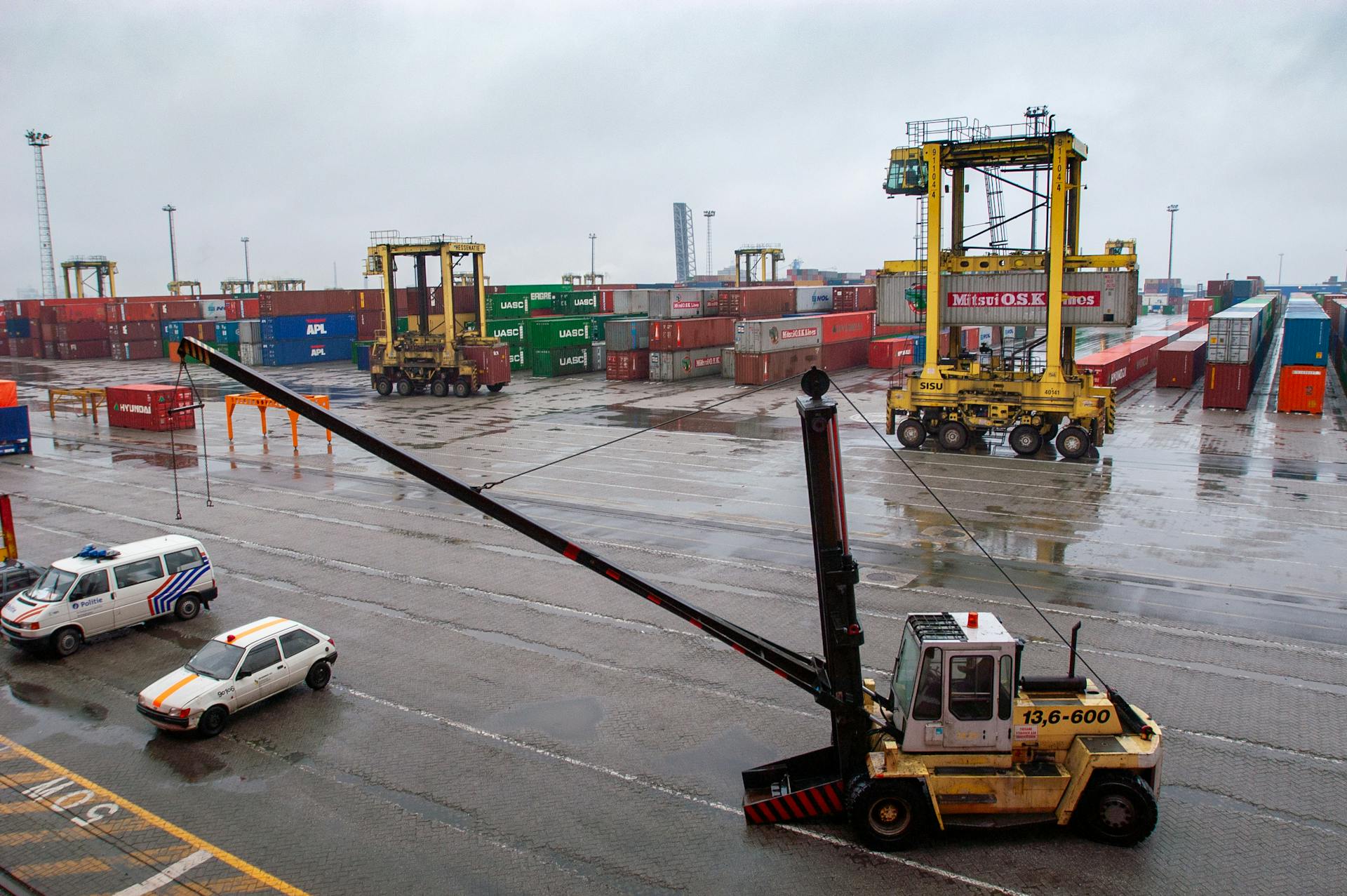 Container terminal with straddle carriers and stacked shipping containers under a cloudy sky.