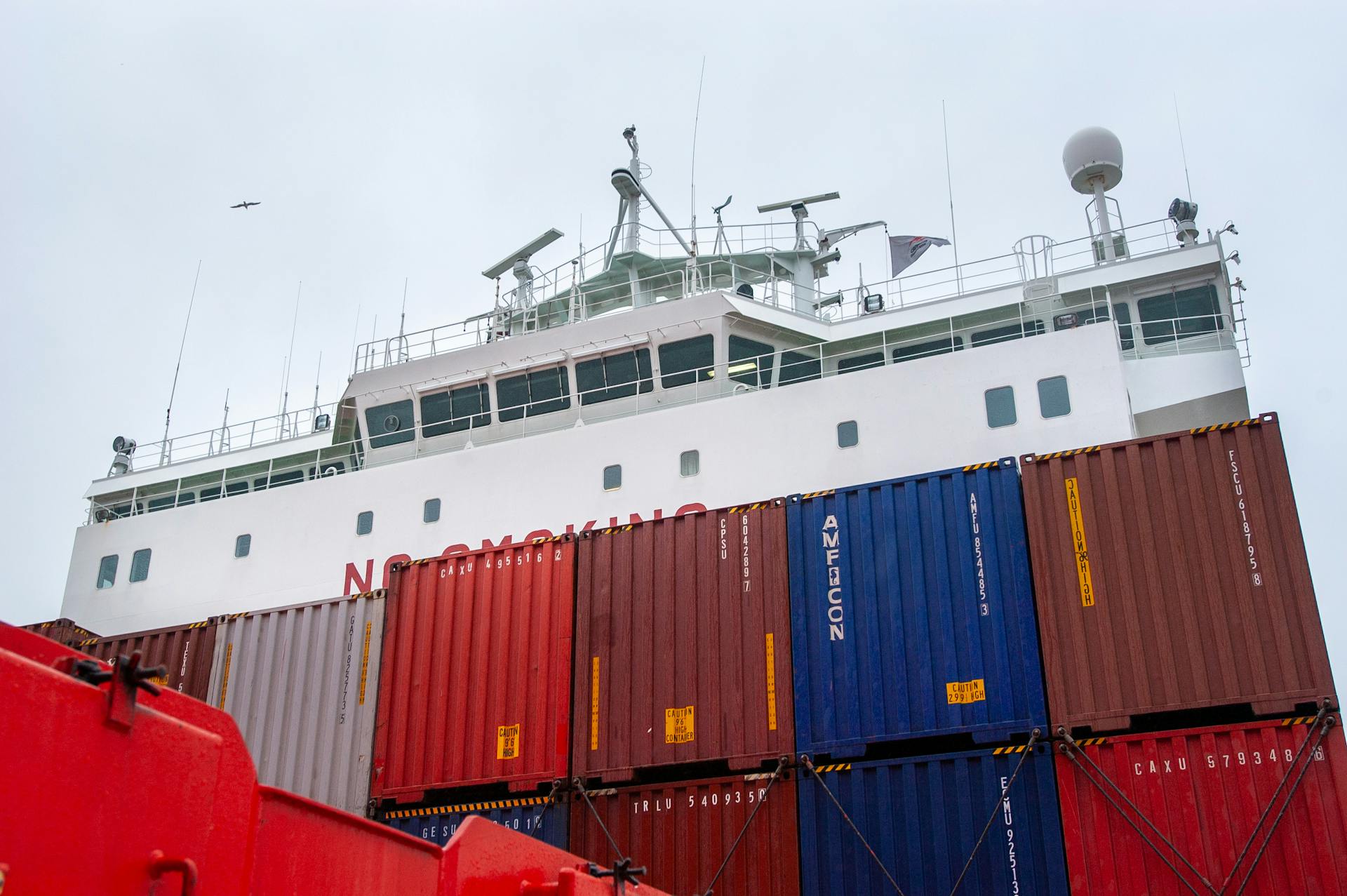 Close-up of a container ship with colorful shipping containers against a cloudy sky.
