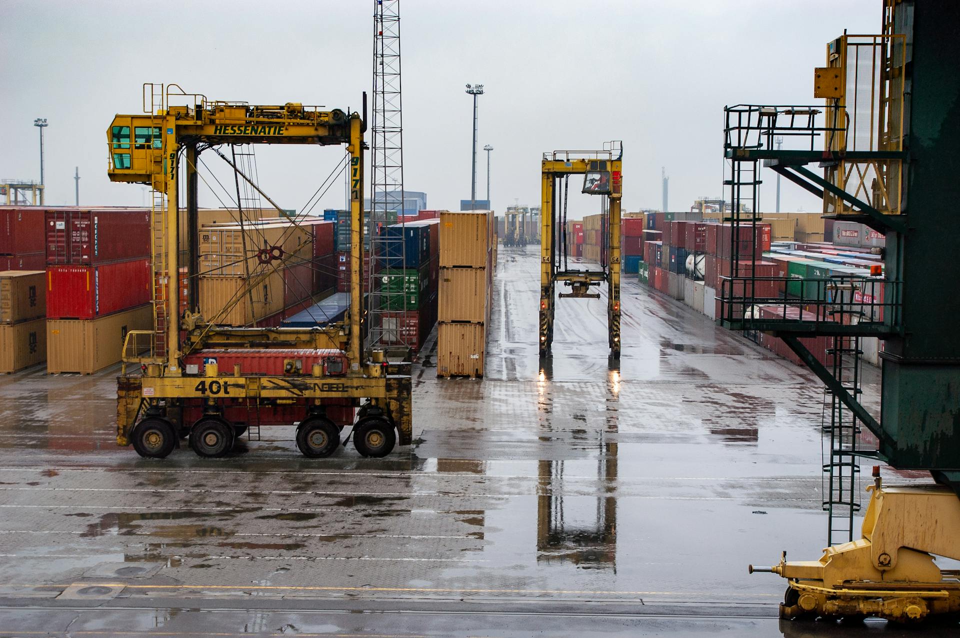 Container yard featuring straddle carriers and stacked containers under a rainy sky.