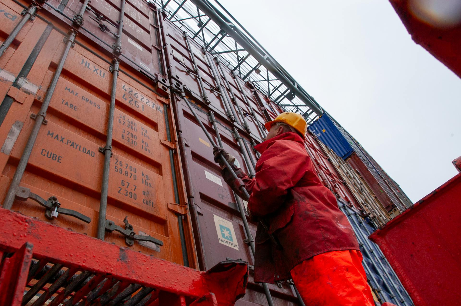 Industrial worker securing cargo containers on a rainy day at a shipping port.